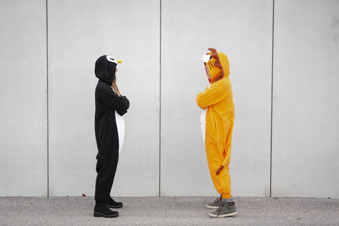 Two women in penguin and lion costume standing opposite in front of concrete wall - HMEF00712