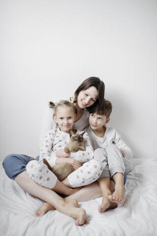Mother with two kids and a cat sitting on bed stock photo