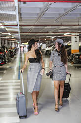 Zwei modische junge Frauen mit Gepäck auf einem Flughafenparkplatz - LJF01178