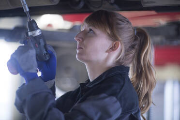 Weiblicher Automechaniker repariert Auto stehend unter dem Boden in der Reparaturwerkstatt - SGF02529