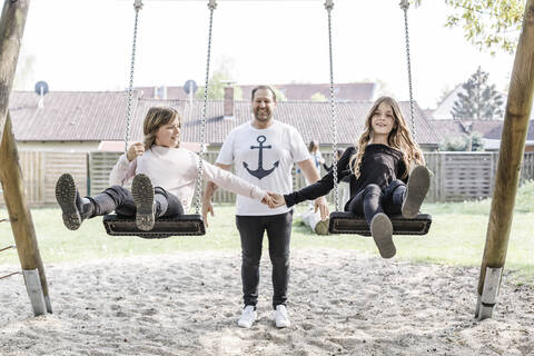 Vater mit zwei Töchtern auf einer Schaukel, lizenzfreies Stockfoto