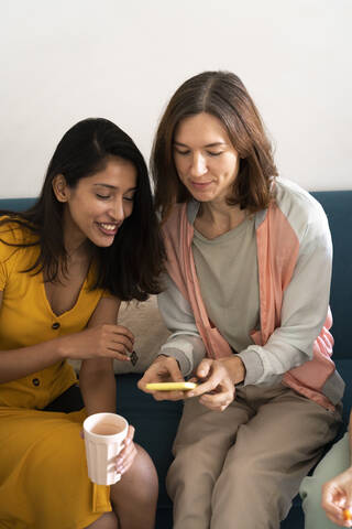 Two women sitting on couch sharing cell phone stock photo