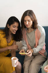 Two women sitting on couch sharing cell phone - AFVF04474