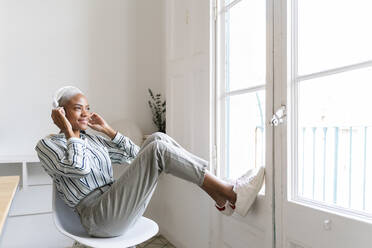 Smiling young woman listening to music at the window - AFVF04497