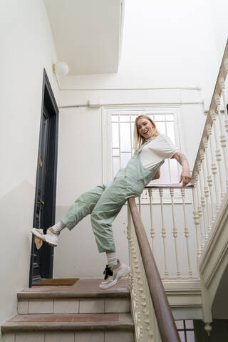 Unbekümmerte junge Frau, die auf dem Geländer im Treppenhaus ausrutscht, lizenzfreies Stockfoto