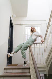 Unbekümmerte junge Frau, die auf dem Geländer im Treppenhaus ausrutscht - AFVF04513