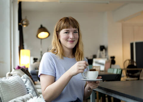 Porträt einer erdbeerblonden jungen Frau mit Nasenpiercing und einer Tasse Kaffee in einem Cafe, lizenzfreies Stockfoto