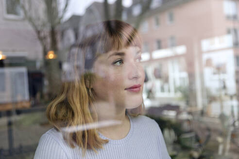 Porträt einer jungen Frau mit Nasenpiercing, die aus dem Fenster schaut - FLLF00366