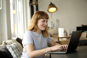 Portrait of strawberry blonde young woman with nose piercing using laptop in a coffee shop - FLLF00367
