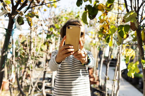 Ein Junge hält ein goldenes Smartphone im Freien in den Händen - VABF02481