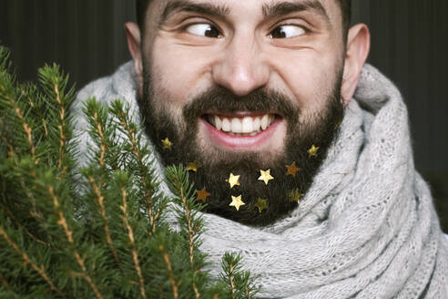 Lustiger Mann mit Weihnachtsbaum und goldenen Sternen in seinem Bart - EYAF00773
