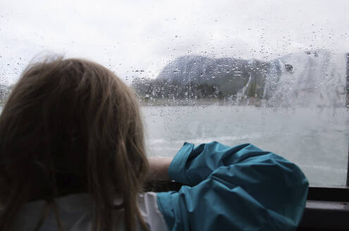 Rückansicht eines Mädchens, das durch ein nasses Fenster schaut - CAVF70814