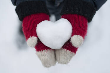 Cropped hands of boy in knitted gloves holding heart shape snow - CAVF70838