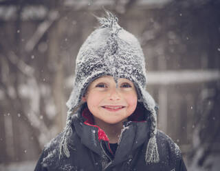 Portrait of cheerful boy wearing hat during snowfall - CAVF70843