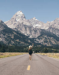 Rear view of woman gesturing while standing on road - CAVF70855