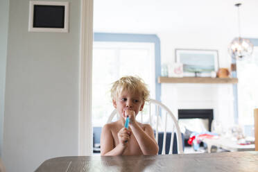Shirtless boy having ice pops tube while sitting at home - CAVF70859