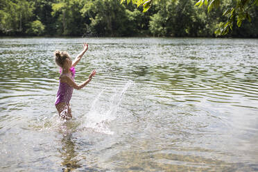 Seitenansicht eines Mädchens, das im See stehend Wasser spritzt - CAVF70862