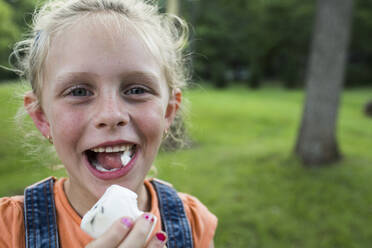 Porträt eines glücklichen Mädchens, das auf einem Feld einen Marshmallow isst - CAVF70864