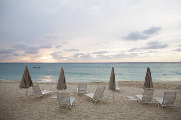 Scenic view of parasols and lounge chairs at beach against cloudy sky - CAVF70870