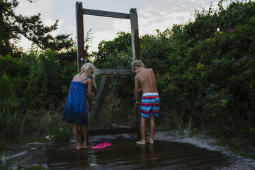 Rückansicht von Geschwistern, die am Tobay Beach ihre Beine im Leitungswasser waschen - CAVF70880