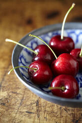 Close-up of cherries in bowl on wooden table - CAVF70907