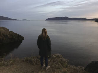 Frau in Jacke mit Blick auf den Fluss und den Himmel - CAVF70942