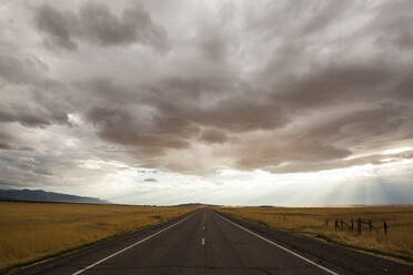 Einspurige Straße inmitten von Feldern gegen stürmische Wolken - CAVF70948
