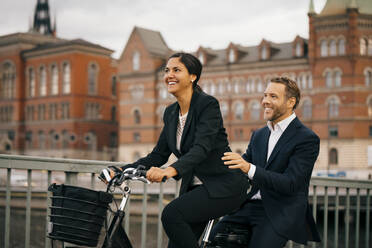 Smiling businesswoman and businessman traveling on bicycle in city - MASF15518