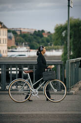Seitenansicht von Geschäftsfrau zu Fuß mit Fahrrad auf Brücke in der Stadt - MASF15519