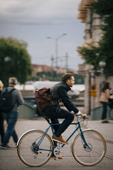 Seitenansicht eines selbstbewussten Geschäftsmannes, der auf einer Straße in der Stadt Fahrrad fährt - MASF15521