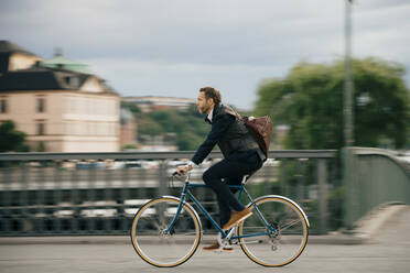 Selbstbewusster Geschäftsmann, der auf einer Brücke Fahrrad fährt, in voller Länge - MASF15525