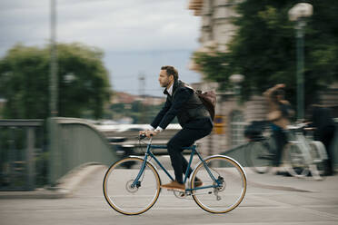 Full length of confident businessman cycling on bridge - MASF15526