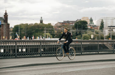 Geschäftsmann fährt Fahrrad auf der Straße in der Stadt gegen den Himmel - MASF15527