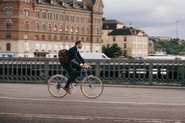 Seitenansicht eines Geschäftsmannes, der auf einer Straße in der Stadt Fahrrad fährt - MASF15529