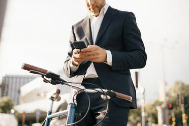 Midsection of businessman using mobile phone while standing by bicycle in city - MASF15540