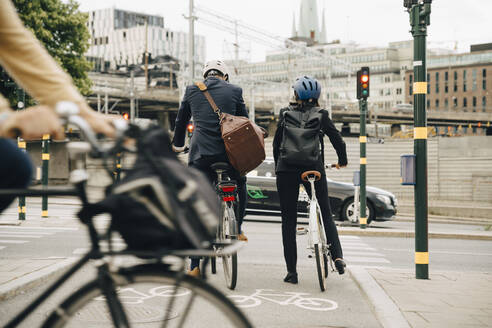 Rückansicht eines Geschäftsmannes und einer Geschäftsfrau mit Fahrrädern auf einer Straße in der Stadt - MASF15548