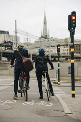 Rear view of businessman and businesswoman with bicycles on city street - MASF15549