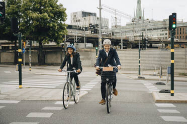 Smiling businessman and businesswoman riding bicycles on road in city - MASF15552