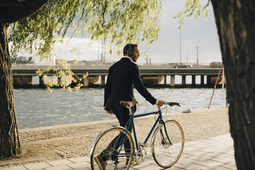 Geschäftsmann zu Fuß mit Fahrrad auf dem Fußweg am Kanal in der Stadt - MASF15558