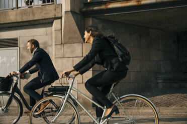 Seitenansicht eines Geschäftsmannes und einer Geschäftsfrau, die auf einer Straße in der Stadt Fahrrad fahren - MASF15566