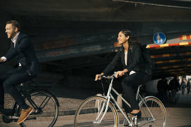 Lächelnder Geschäftsmann und Geschäftsfrau auf Fahrrädern auf der Straße in der Stadt - MASF15567
