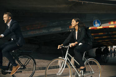 Smiling businessman and businesswoman riding bicycles on street in city - MASF15567