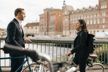 Lächelnde Geschäftsfrau im Gespräch mit Geschäftsmann auf Brücke beim Radfahren in der Stadt - MASF15577
