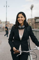 Portrait of smiling businesswoman with bicycle on bridge in city - MASF15590