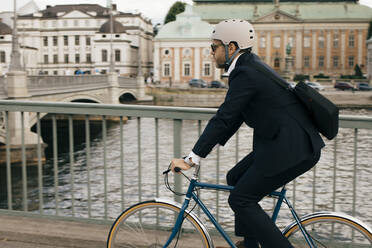 Side view of businessman riding bicycle on bridge by canal in city - MASF15592