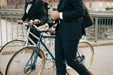 Midsection of businessman and businesswoman walking with bicycles on bridge in city - MASF15596