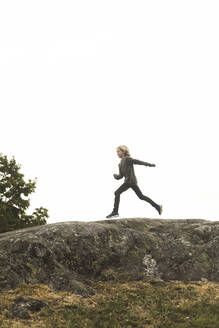 Full length side view of girl running on rock formation against clear sky - MASF15600