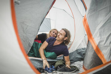 Paar späht durch das Zelt, während es sich im Schlafsack beim Camping anlehnt - MASF15615