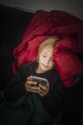 Hochformatige Ansicht eines Mädchens, das ein Mobiltelefon benutzt, während es im Zelt liegt - MASF15622