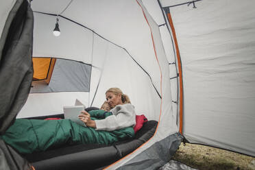Mutter und Tochter benutzen ein digitales Tablet, während sie im Zelt auf dem Campingplatz liegen - MASF15623